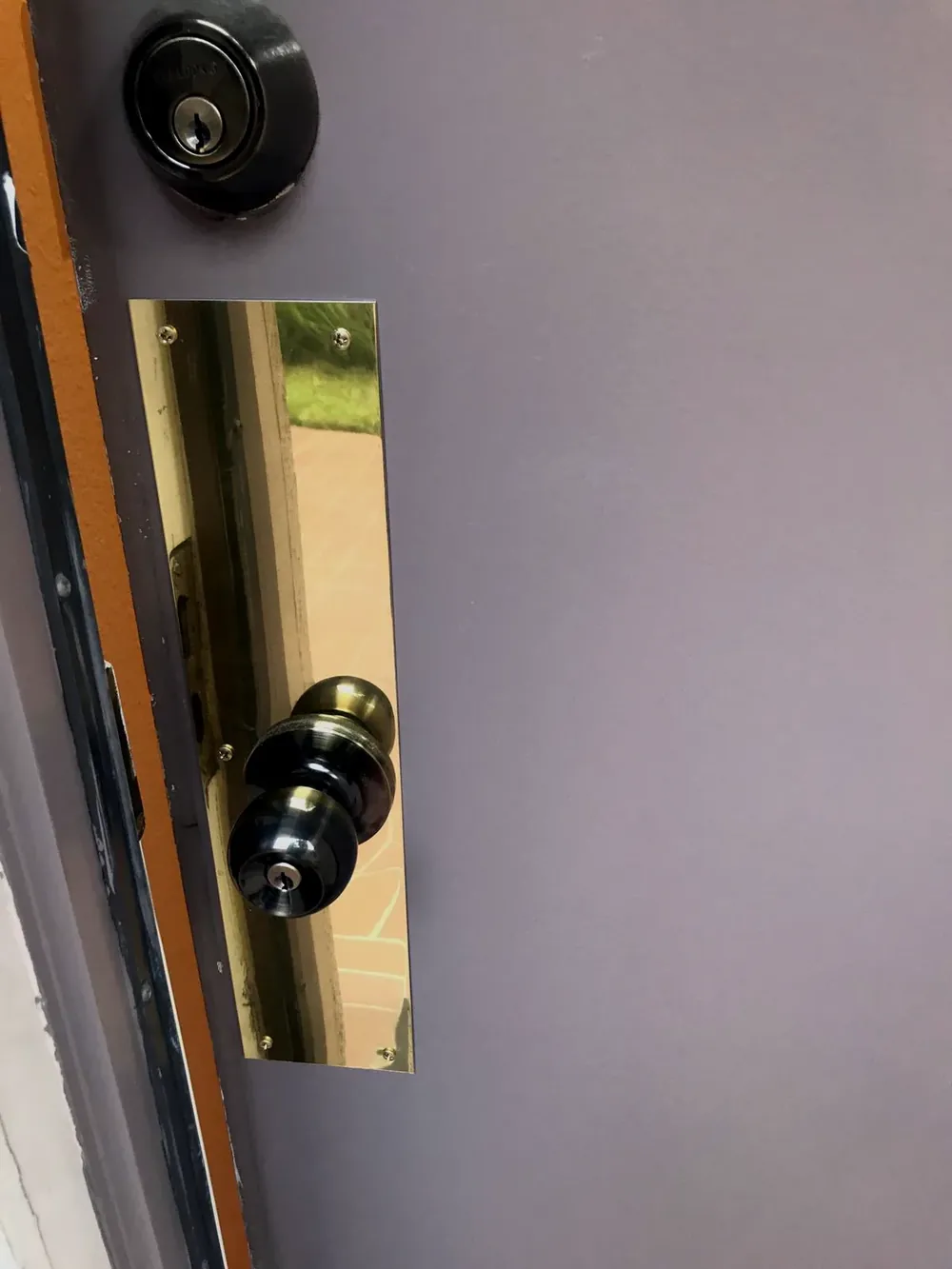 Deadbolt and knob lock with a brass kick plate on a gray shop door