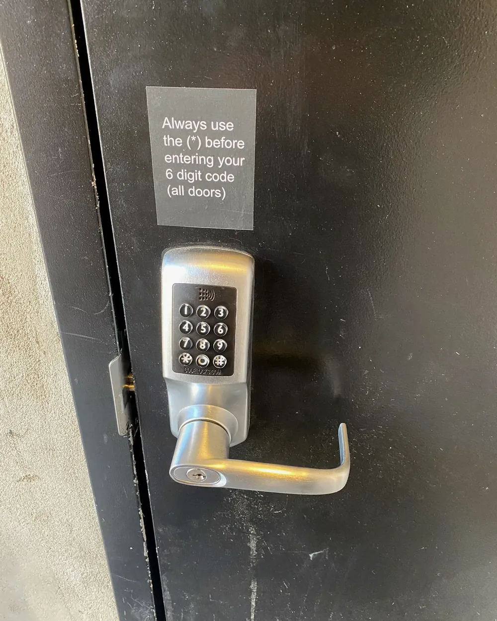 Keypad lever lock on a dark commercial door with a code instruction sign