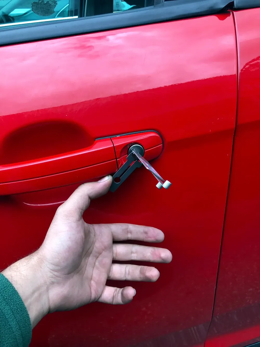 Locksmith opening a locked red car door with a lockout tool