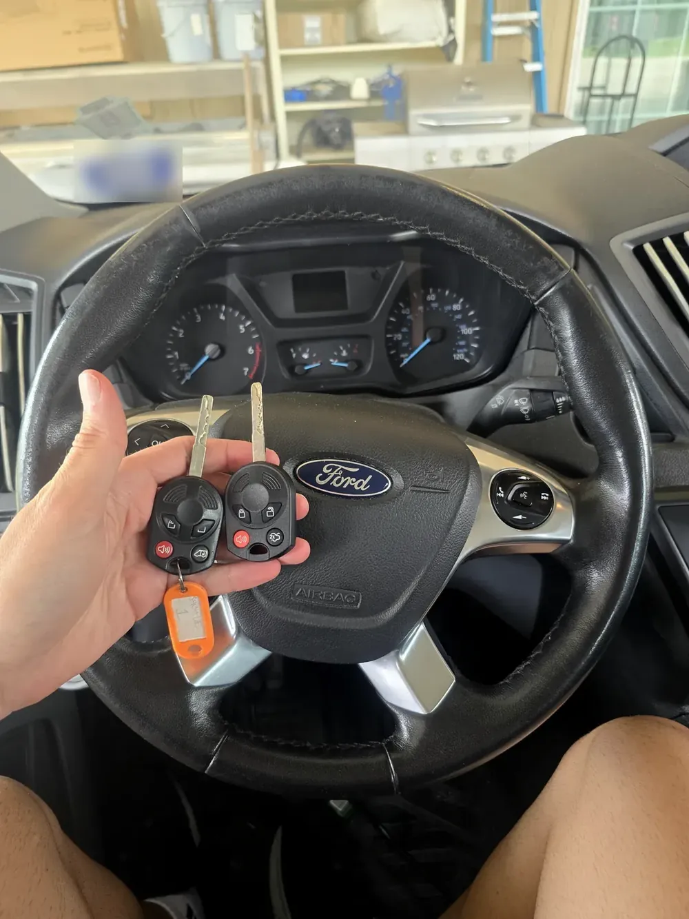 Two new Ford keys held at the steering wheel of a Ford Transit work van