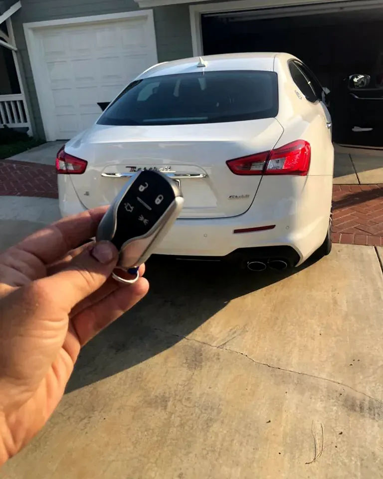 New Maserati smart key held behind a white Maserati in a home driveway after a job in Oceanside, NY