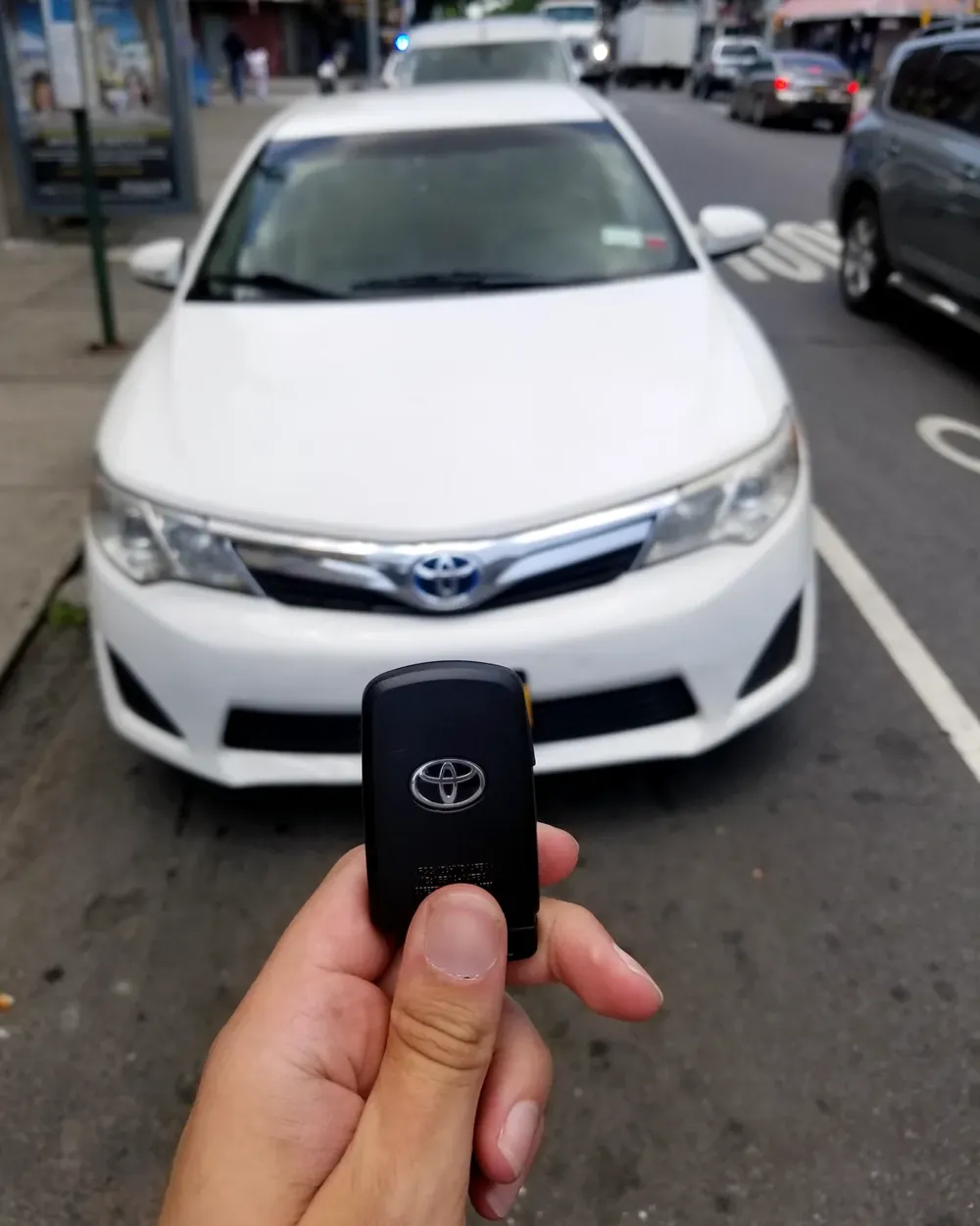 New Toyota smart key held in front of a white Toyota parked on the street
