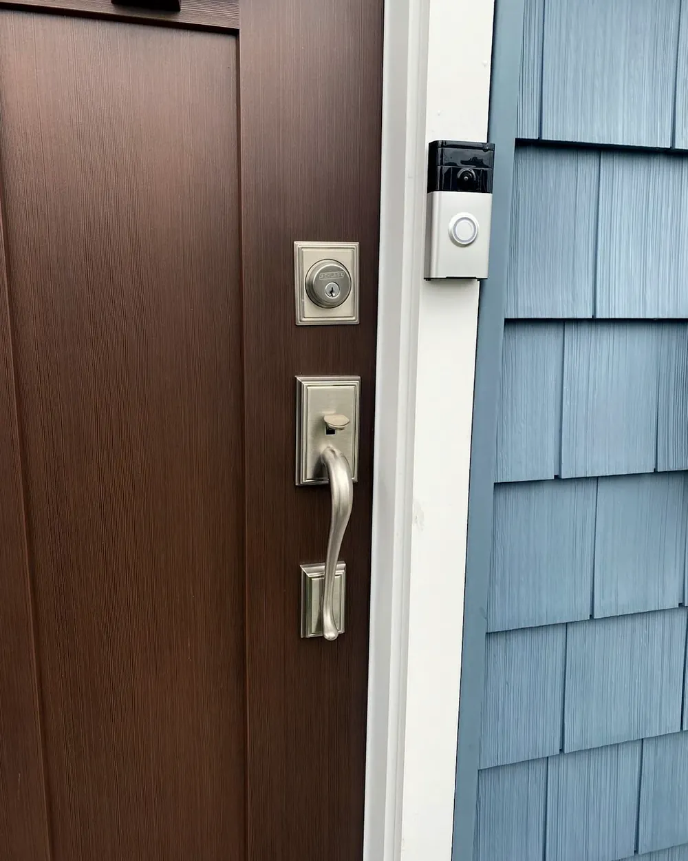 Satin handleset and deadbolt on a wood front door next to shingle siding