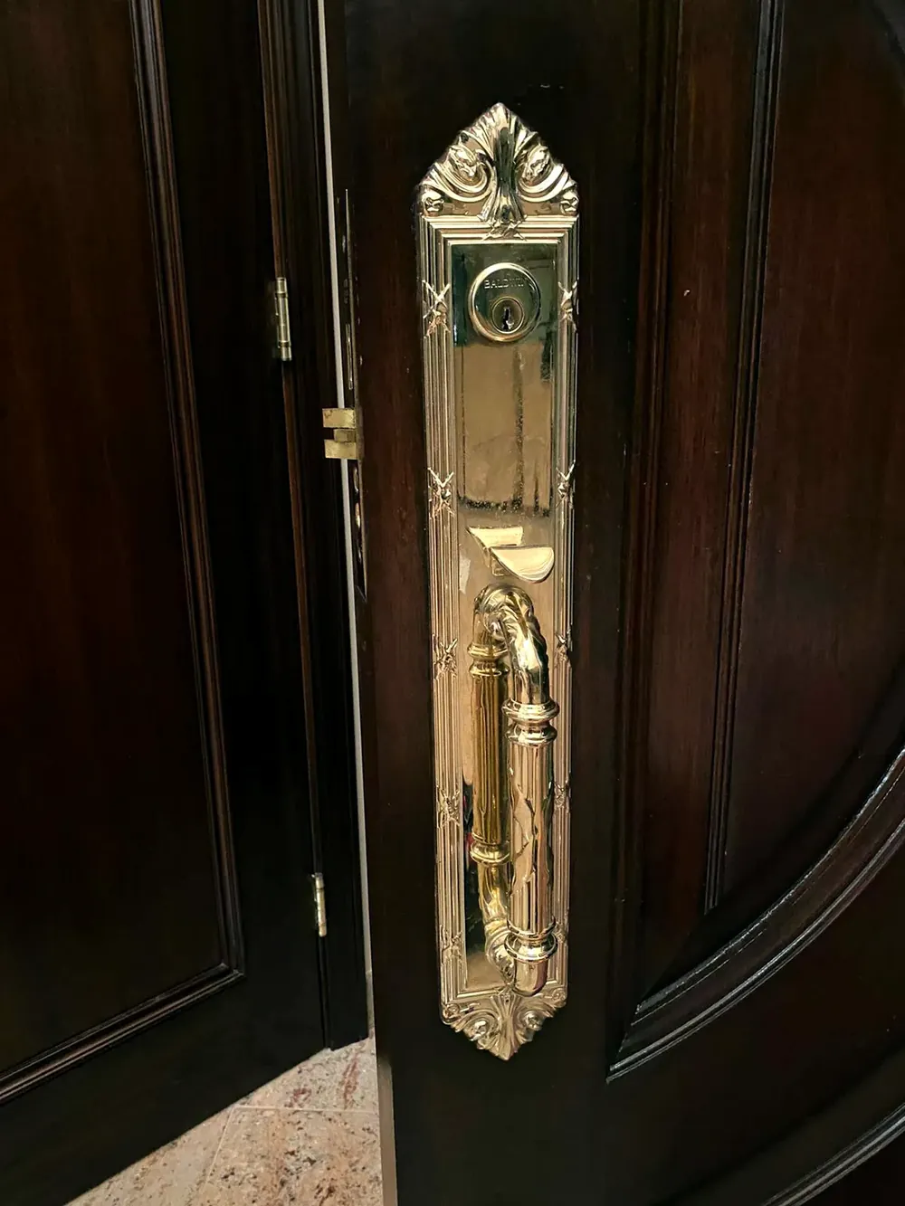 Brass handleset with a thumb latch and deadbolt on a dark wood front door